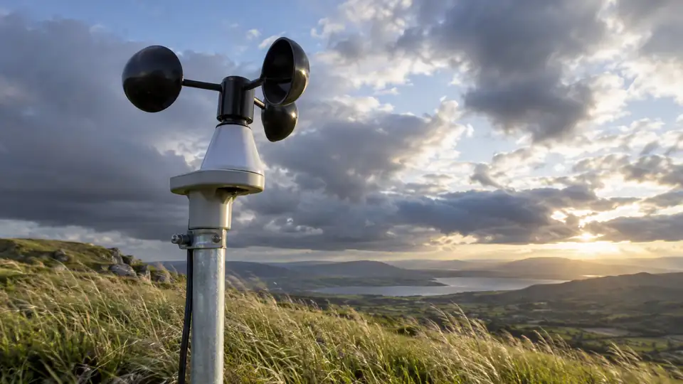 Weather station anemometer measuring wind above an open hillside.